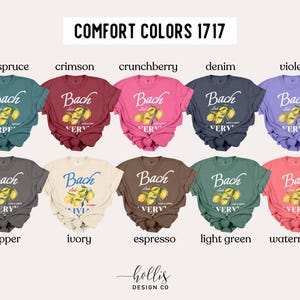 May include: A collection of Comfort Colors 1717 t-shirts in various colors, including blue spruce, crimson, crunchberry, denim, and violet. Each shirt features the text "Bach Club" with a lemon graphic. Additional colors include pepper, ivory, espresso, light green, and watermelon.