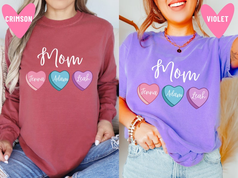 May include: Two long-sleeved shirts with the word "Mom" and three candy hearts with names "Jenna", "Adam", and "Leah". The shirt on the left is crimson and the shirt on the right is violet.