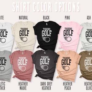 May include: A set of ten t-shirts in various colours, each featuring a graphic of a golf ball with the text "TIGERS GOLF". The colours include white, natural, black, pink, ash, athletic heather, heather mauve, dark grey heather, heather peach, and heather olive.