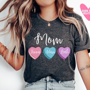 May include: A dark grey heather t-shirt with the word "mom" printed in white cursive. Three candy hearts with the names "Jenna", "Adam", and "Leah" are printed below the word "mom".