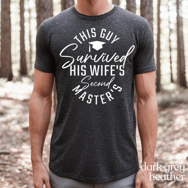 May include: Dark grey heather t-shirt with white text that reads "This Guy Survived His Wife's Second Master's". A graduation cap icon is above the word "Survived".