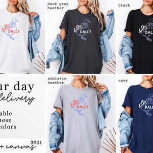 May include: Five different coloured t-shirts: white, dark grey heather, black, athletic heather, and navy. Each shirt has a duck graphic with the words "dilly dally". The shirts are from Bella + Canvas.