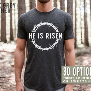 May include: A dark grey heather t-shirt with a white crown of thorns design and the text "He is Risen". The shirt is available in 30 options, including t-shirt, long sleeve, and sweatshirt.