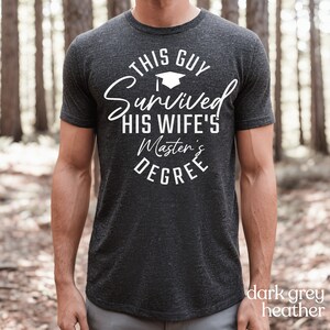 Peut inclure: T-shirt gris fonc&eacute; chin&eacute; avec un texte blanc qui dit "This Guy Survived His Wife's Master's Degree".