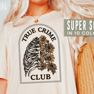 May include: A white t-shirt with a graphic of a ribcage and flowers. The text "TRUE CRIME CLUB" is printed on the shirt. The shirt is super soft and available in 10 colors.