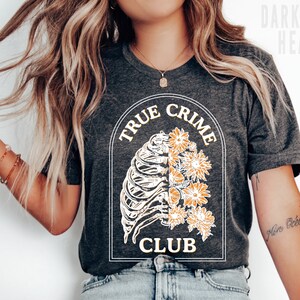 May include: A dark grey heather t-shirt with a graphic of a ribcage with flowers and the text "True Crime Club".