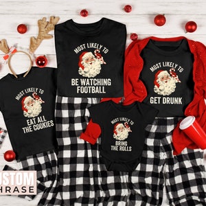 May include: Four black t-shirts with a Christmas theme. Each shirt features a cartoon image of Santa Claus with a candy cane and text that says "Most Likely To" followed by a funny Christmas-themed phrase. The phrases are "Eat All The Cookies", "Be Watching Football", "Bring The Rolls", and "Get Drunk".