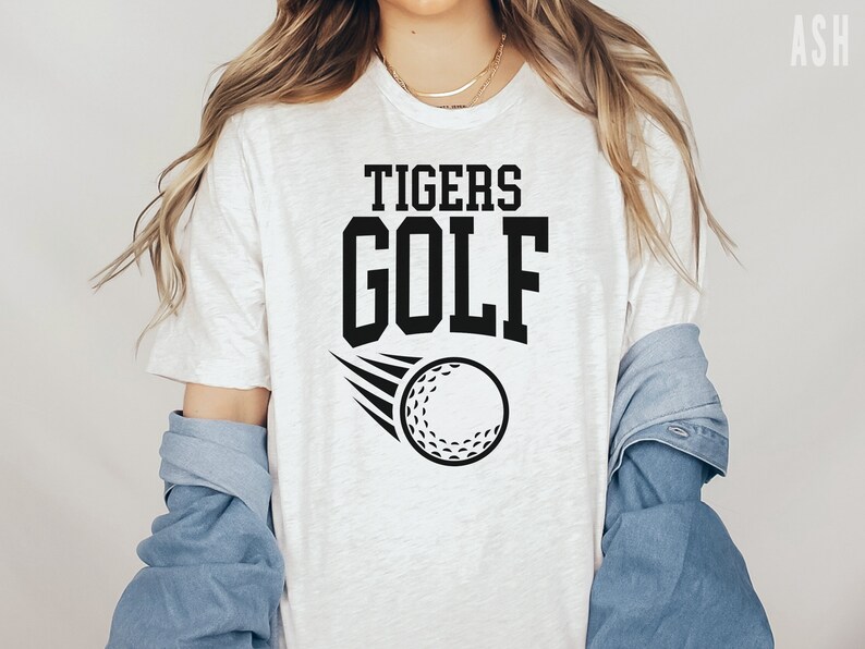 May include: White t-shirt with black text that reads "TIGERS GOLF" and a black and white golf ball graphic.