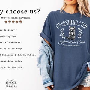 Puede incluir: Camiseta azul marino con el texto "OVERSTIMULATED Antisocial Club SLIGHTLY UNHINGED" y un gr&aacute;fico de mapache. La persona lleva una chaqueta vaquera. La imagen tambi&eacute;n incluye texto sobre el vendedor.