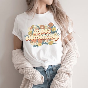 May include: White t-shirt with a retro-style graphic that says "upper elementary" surrounded by colorful flowers.
