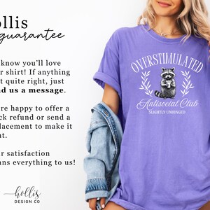 Puede incluir: Camiseta violeta con el texto "OVERSTIMULATED Antisocial Club SLIGHTLY UNHINGED" y un gr&aacute;fico de mapache. La camiseta tiene un corte relajado y est&aacute; hecha de un material suave. Parte de una colecci&oacute;n de ropa.