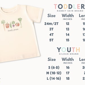 May include: Cream-colored toddler t-shirt with a colorful illustration of vegetables and the text "locally grown." Size chart for toddler and youth sizes is included. The shirt is from the Rabbit Skin and Gildan brands.
