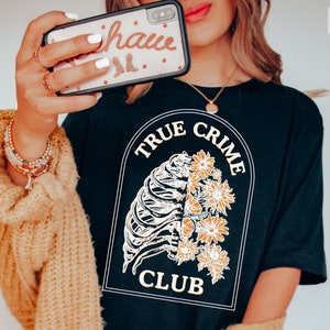 May include: Black t-shirt with a white graphic of a ribcage with flowers and the text "True Crime Club".