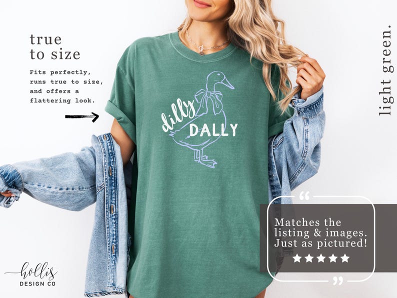 May include: A light green t-shirt featuring a white outline of a duck and the words "dilly dally". The shirt has rolled-up sleeves and is made of a soft material. The text "true to size" is also visible.