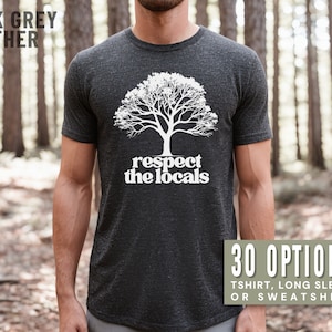 May include: A dark grey heather t-shirt with a white tree and the text "respect the locals" in a retro font. The shirt is being worn by a person in a forest setting. 30 options: t-shirt, long sleeve or sweatshirt.