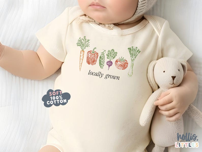 May include: Cream-colored baby bodysuit with a vegetable graphic and the words "locally grown." The design includes a carrot, bell pepper, pea, beet, tomato, and leek. The bodysuit is labeled "Soft 100% Cotton."