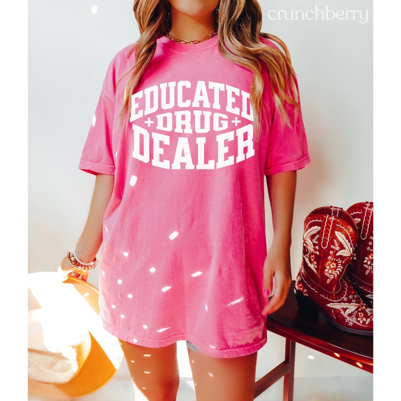 Op de afbeelding: Een oversized roze T-shirt met de tekst "EDUCATED + DRUG + DEALER" in witte letters.