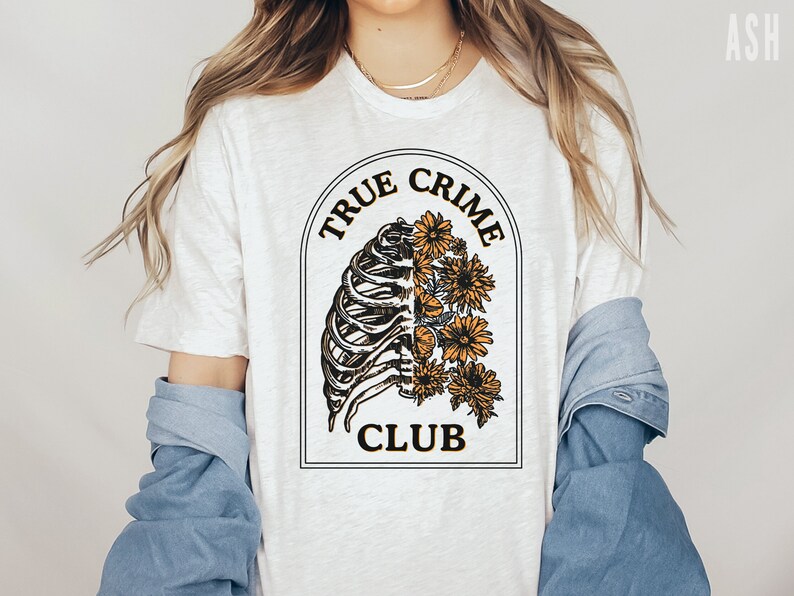 May include: White t-shirt with a graphic of a ribcage with flowers growing out of it. The graphic is surrounded by a black circle with the text "True Crime Club" in black and yellow lettering.