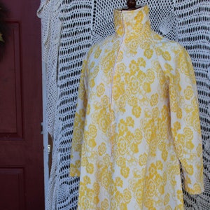 May include: A long white robe with a yellow floral pattern and a zipper closure. The robe has long sleeves and a collar.