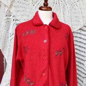 May include: Red fleece jacket with a button-up front and a collar. The jacket features a floral design with small white and black accents.
