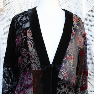 May include: A black velvet jacket with a patchwork design featuring various shades of purple, red, and gold. The jacket has a long sleeve and a V-neckline.