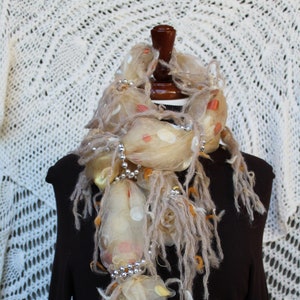 Może przedstawiać: Beżowo-brązowy szal z przezroczystego materiału z akcentami pereł. Szal jest drapowany wokół szyi manekina.