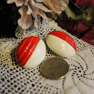 Op de afbeelding: Een paar ovale oorbellen in rood en wit. De oorbellen zijn gemaakt van plastic en hebben een glanzende afwerking.