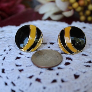 May include: A pair of gold tone earrings with black and yellow enamel. The earrings are round and have a simple design.