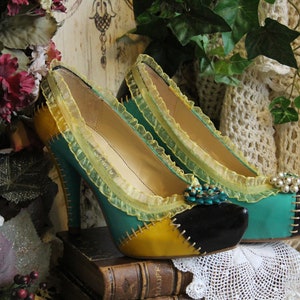 May include: A pair of high-heeled shoes with a green, yellow, and black patchwork design. The shoes have a yellow lace trim and a black toe cap. The shoes are sitting on a stack of books.