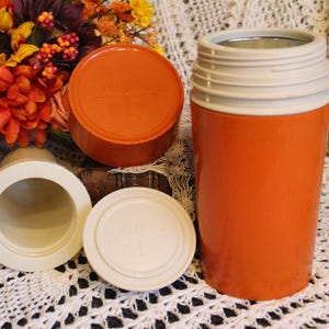 May include: A set of four orange and white thermoses with lids. The thermoses are made of plastic and have a vintage look.