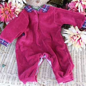 May include: A burgundy velour baby onesie with a plaid collar and cuffs. The onesie has a button closure at the neck and a snap closure at the crotch.