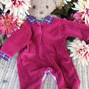 May include: A plush teddy bear wearing a burgundy velvet jumpsuit with a plaid collar and a straw hat with floral embellishments.