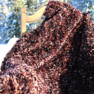 Pode incluir: Uma manta de pelo marrom e preto drapeada sobre uma cadeira de madeira. A manta é feita de um material macio e felpudo e tem uma aparência texturizada.