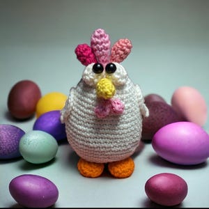 Puede incluir: Un pollo hecho a mano, tejido a ganchillo, con cuerpo blanco, cresta rosa y roja, pico amarillo y patas naranjas. El pollo está rodeado de coloridos huevos de Pascua en tonos morado, rosa, amarillo y verde. El fondo es de un color suave y neutro.