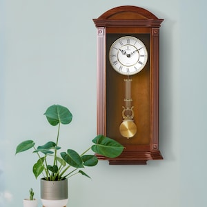 May include: A traditional wooden pendulum clock with a Roman numeral clock face and a gold-colored pendulum. The clock is mounted on a wall and has a light wood finish.