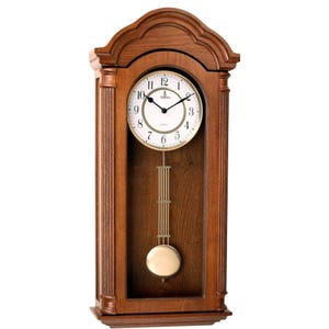 May include: A wooden wall clock with a brown finish, featuring a white circular face with black Arabic numerals and hands. The clock includes a gold-toned pendulum suspended behind a glass panel, framed by fluted columns and an arched top.