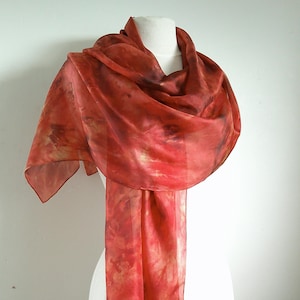 May include: A long, flowing red silk scarf with a tie-dye pattern. The scarf is draped over a white mannequin.