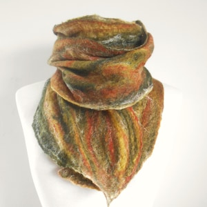 May include: A felted scarf in shades of brown, green, orange, and yellow, displayed on a white mannequin. The scarf has a textured, layered design, with a triangular shape at the bottom. The colors blend together, creating a warm, earthy aesthetic. The scarf appears to be handmade.