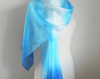 May include: A blue and white ombre scarf draped over a mannequin. The scarf transitions from white to light blue to a deep blue at the ends. The scarf is made of a sheer, lightweight fabric.