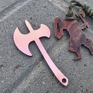 Könnte beinhalten: Zwei metallene Flaschenöffner in Axtform. Einer ist eine traditionelle Axtform mit rosafarbener Oberfläche. Der andere ist eine Silhouette einer Person, die eine Axt mit brauner Oberfläche hält.