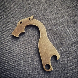 May include: A brass bottle opener shaped like a dragon's head with a cutout for opening bottles.