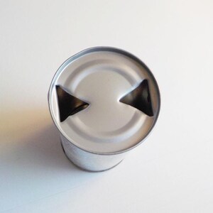 Puede incluir: Una lata de plata con una tapa de leng&uuml;eta. La leng&uuml;eta tiene dos recortes triangulares.