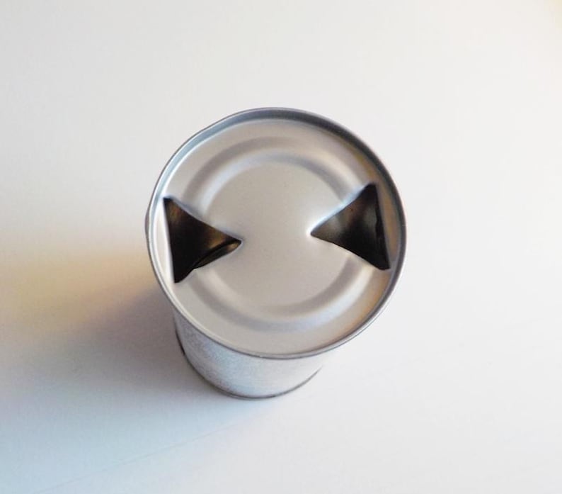 Puede incluir: Una lata de plata con una tapa de leng&uuml;eta. La leng&uuml;eta tiene dos recortes triangulares.