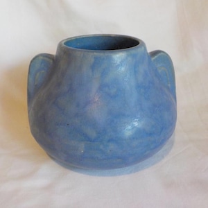 May include: A small, round ceramic vase with a matte blue finish and a mottled, cloud-like texture. The vessel features two integrated side handles and a wide, circular opening at the top, showcasing a consistent blue color throughout the body.