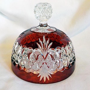 May include: A dome-shaped glass cover featuring a deep red color with clear, cut-glass detailing. The surface displays a diamond-cut pattern and vertical fan motifs. A clear, textured glass knob sits at the top of the dome for easy handling.