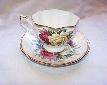 May include: White teacup and saucer set with a floral rose design in shades of red, yellow, and pink. The edges of the cup and saucer are scalloped and trimmed with gold. A classic and elegant tea set.