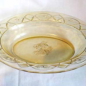 May include: An oval, yellow glass serving bowl with a vintage aesthetic. The rim has a repeating geometric and floral pattern. The centre of the bowl features a raised floral design. Suitable for serving food, this bowl is a decorative piece.