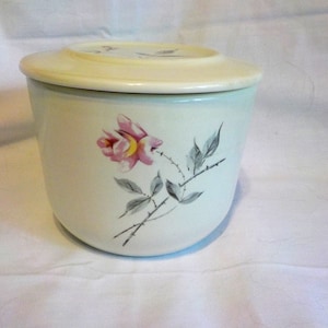 May include: A vintage, off-white ceramic butter dish with a matching lid. The dish features a hand-painted pink rose with gray leaves and thorns. The lid is a lighter shade of cream.