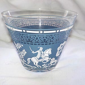 May include: A clear glass bowl with a blue band featuring a white equestrian scene and decorative patterns. The bowl has a flared shape and is likely vintage, suitable for serving or display.