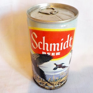 May include: Vintage Schmidt Beer can with a red and white label. The label features the brand name and a graphic of flying pheasants over a field. The can has a silver top and a light blue body.